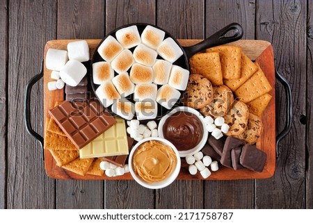 Smores platter. Roasted marshmallows, crackers, chocolate and a group of ingredients. Above view on a dark wood background. Royalty-Free Stock Photo #2171758787