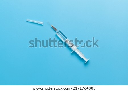 Medical syringe for liquid 5 ml. White medical syringe with a cap, isolated on a blue background. Royalty-Free Stock Photo #2171764885