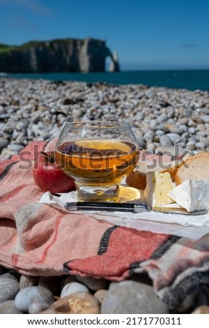 Lunch on pebbles beach of Etretat, french cheese camembert, fresh baked  baguette and apple cider drink with chalk cliffs and Atlantic ocean on background, Normandy, France