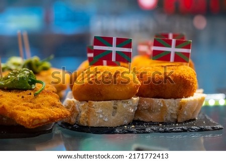 Typical snack in bars of Basque Country, pinchos or pinxtos, small fried croquette with squid and flag of Basque Country, San Sebastian, Spain, close up