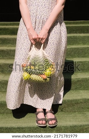 Knitted mesh bag with vegetables and fruits in the hands of a woman. Zero waste grocery shopping concept.