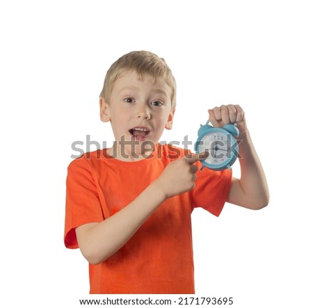 a boy in an orange T-shirt is holding an alarm clock and pointing his finger at the time on the alarm clock. white background. copy sapace.