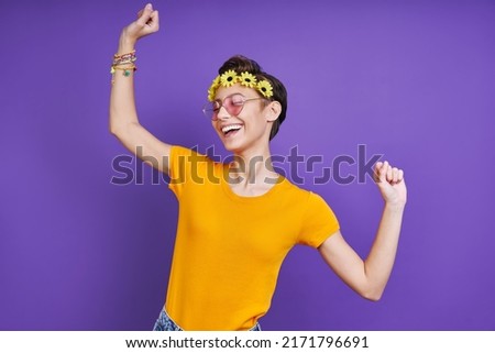 Cheerful young woman with floral head wreath gesturing while standing against purple background