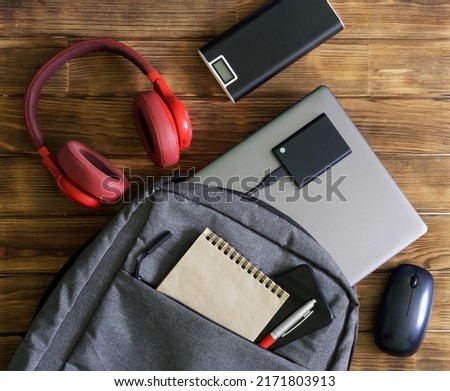 Modern gadgets and gray textile backpack or bag on wooden table. Laptop, portable ssd, smartphone, notepad, pen, headphones, mouse and external battery - poverbank. For work and study. Close-up Royalty-Free Stock Photo #2171803913