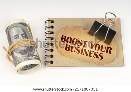 Business and finance concept. On a white surface are twisted dollars, a notebook and a cardboard sign with the inscription - BOOST YOUR BUSINESS