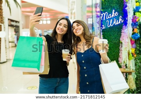 Happy women friends drinking coffee and taking a selfie while shopping at the mall 