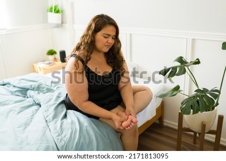 Ill obese woman with pain in her foot. Big woman rubbing her feet because of muscle cramps while sitting in bed