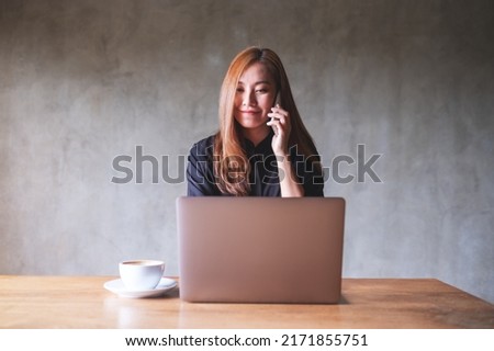 Portrait image of a businesswoman using and talking on mobile phone while working on laptop computer