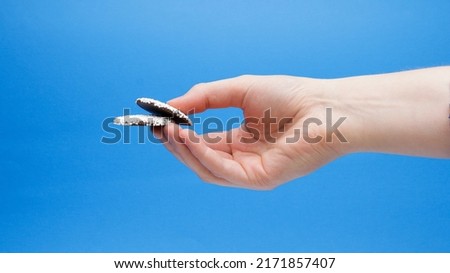 Two Dark Chocolate Nonpareils In Hand On A Blue Background