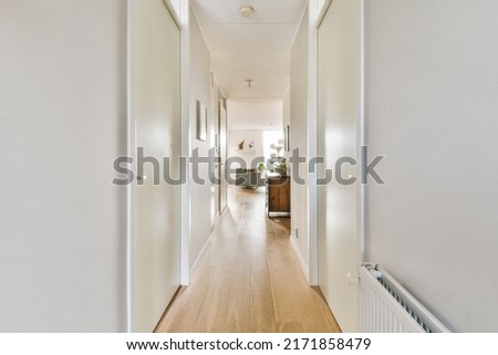 Narrow corridor with white walls and doors leading to spacious room with windows and parquet floor in modern apartment Royalty-Free Stock Photo #2171858479