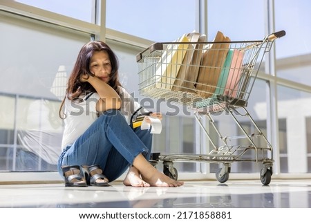 Worried asian businesswoman shopping plenty of clothes and products, holding mock up credit cards and bill to clear up a charge on her credit card with hand on head, sad and angry face.   Royalty-Free Stock Photo #2171858881