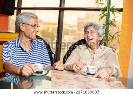 Happy indian senior couple sitting in living room with cup of tea or coffee laughing and talking, Retired old man and woman enjoying spend time together at home. Royalty-Free Stock Photo #2171859887