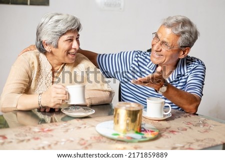 Happy old indian  couple sitting in living room with cup of tea or coffee laughing and talking, Retired elderly man and woman enjoying spend time together at home. Royalty-Free Stock Photo #2171859889