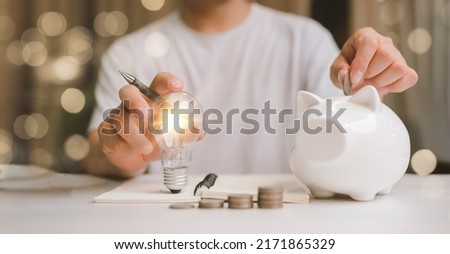 business man hand holding lightbulb and putting coin in to the piggy bank. idea saving energy and accounting finance in home and family concept, save world and energy power. Royalty-Free Stock Photo #2171865329