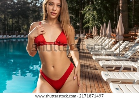 Young blond woman in sunglasses and red swimsuit relaxing  and posing against swimming pool at resort