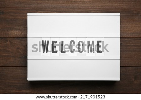 Lightbox with word Welcome on wooden background, top view
