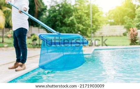 Man cleaning the pool with the Skimmer, A man cleaning pool with leaf skimmer. Person with skimmer cleaning pool, Hands holding a skimmer with blue pool in the background Royalty-Free Stock Photo #2171903009