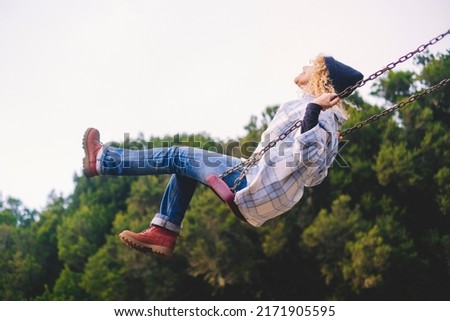 Joyful and youthful woman flying high on a swing at the childhood park. Concept pf people and no limit age to play and have fun. Female in outdoors leisure activity using swing and enjoy life Royalty-Free Stock Photo #2171905595