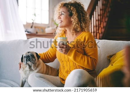 Happy female dog owner smile and enjoy happy time at home with her best friend old pug sitting near her. Animal and love therapy with people. Adult woman have care of her puppy and drink a tea Royalty-Free Stock Photo #2171905659