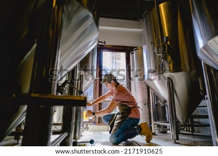 Young male brewer holding a glass of beer in hand Eating craft beer to check the taste and color of the beer in the craft brewery.