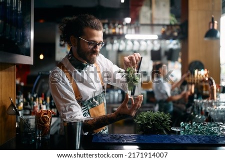 Young happy barmen preparing mojito cocktail and adding mint leaf in a glass at bar counter. Royalty-Free Stock Photo #2171914007
