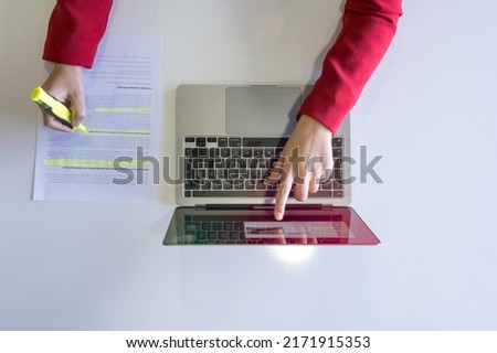 Holding highlighter pen, top view of woman hand holding highlighter pen. Working on laptop and highlighting or marking important text on working paper, isolated on white desk. Royalty-Free Stock Photo #2171915353