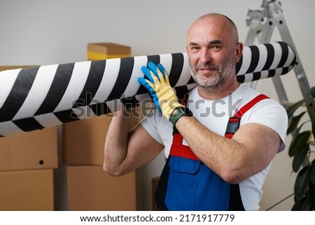 Man mover in uniform carrying big rolled carpet for relocation Royalty-Free Stock Photo #2171917779