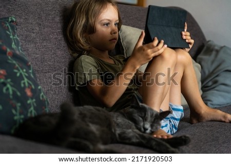 Boy sitting on sofa using digital tablet computer playing games or watching cartoons at home. Child internet safety concept. Kid using electronic equipment. Parental control. Online education.