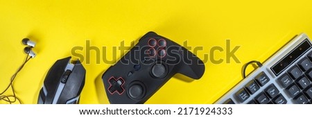Gaming concept with various gamers devices on bright yellow background - gamepad joystick, keyboard, mouse, headphones. Girls gamer concept with gaming technics in woman hands, flatlay copy 