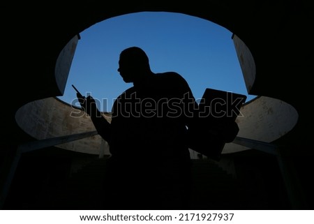 silhouette of Man uses smartphone on stairway. blue sky on background. business male holding in hands smart phone and laptop. Royalty-Free Stock Photo #2171927937