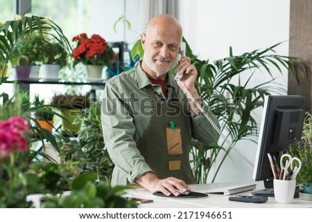 Professional florist working in his shop, he is taking orders over the phone and using a computer Royalty-Free Stock Photo #2171946651