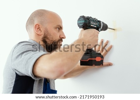 Professional handyman using a drill and drilling a hole in the wall Royalty-Free Stock Photo #2171950193