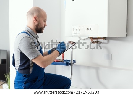 Gas engineer writing a gas safety certificate and boiler records after servicing Royalty-Free Stock Photo #2171950203