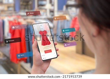Shopping with smart phone and augmented reality app in the boutique concept. Trying on the latest clothes of different sizes and colors. Woman holding smart phone Royalty-Free Stock Photo #2171953739