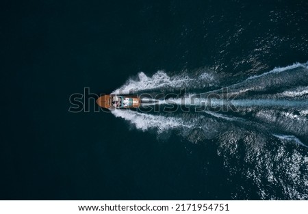 Modern wooden boat in a classic design, moving on water, aerial view. Luxurious wooden boat with people moves on dark water top view. Italian classic wooden boat fast movement on the water top view. Royalty-Free Stock Photo #2171954751