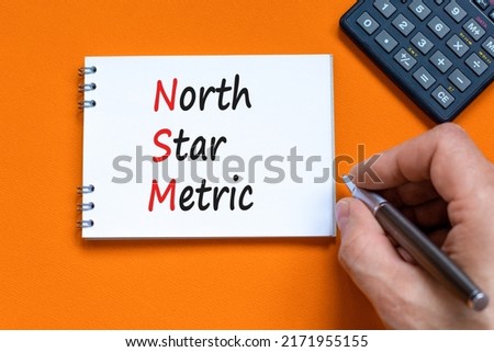 NSM north star metric symbol. Concept words NSM north star metric on white note on a beautiful orange background. Businessman hand. Business and NSM north star metric concept. Copy space.