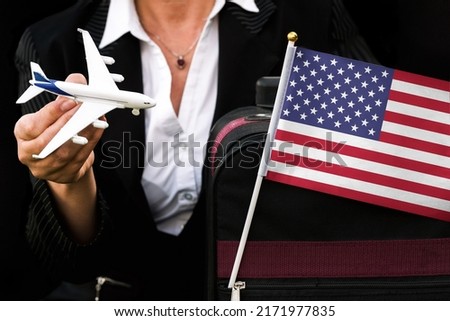 business woman holds toy plane travel bag and flag of United States 