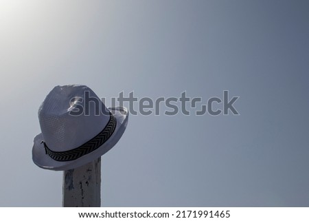 Close-up of a hat hanging on a pole against a blue sky. A white hat hanging from some old pole on the beach. A girl's hat hanging on a wooden pole from a cedar fence.
