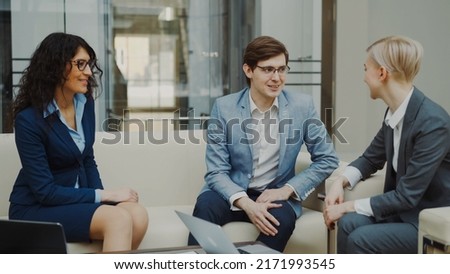 Businessman in glasses talking and duscussing future contract with female business partners sitting on couch in meeting room indoors