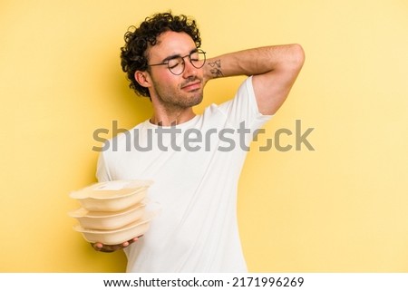 Young caucasian man holding tupper isolated on yellow background touching back of head, thinking and making a choice.