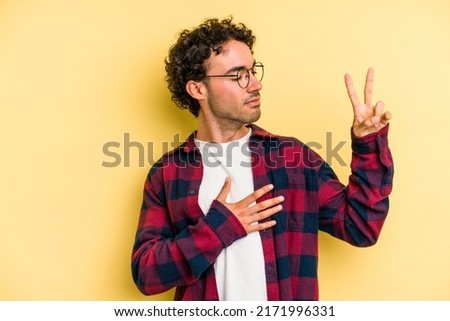 Young caucasian man isolated on yellow background taking an oath, putting hand on chest. Royalty-Free Stock Photo #2171996331