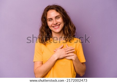 Young caucasian woman isolated on purple background has friendly expression, pressing palm to chest. Love concept.