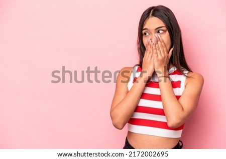 Young hispanic woman isolated on pink background thoughtful looking to a copy space covering mouth with hand.