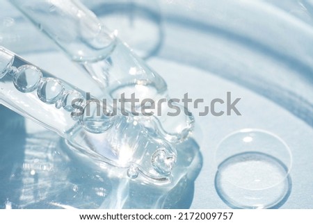 Two pipettes with transparent cosmetic liquid over blue background with copy space. Texture of face serum or cosmetic oil, beaty treatment. Selective focus Royalty-Free Stock Photo #2172009757