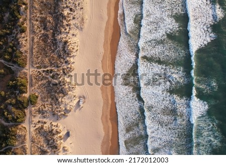 Aerial view over the clear beach and blue water of Fonte da Telha, Portugal. Top down shot of empty sandy ocean coast with huge waves Royalty-Free Stock Photo #2172012003