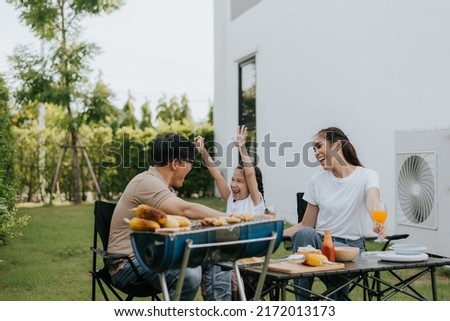 Asian family having dinner in the backyard at home. Happy family with little child camping and have fun in house backyard outside. Barbecue time, Family activities conccept. Royalty-Free Stock Photo #2172013173
