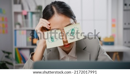 Young Asian businesswoman sitting on desk overworked tired sleep over a laptop at office. Exhausted burnout lady  with two post-it over her eyes, adhesive notes on face sleeping at workplace. Royalty-Free Stock Photo #2172017991
