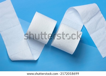 Two rolls of toilet paper lie unwound in different directions on a blue and light blue background.  View from above Royalty-Free Stock Photo #2172018699