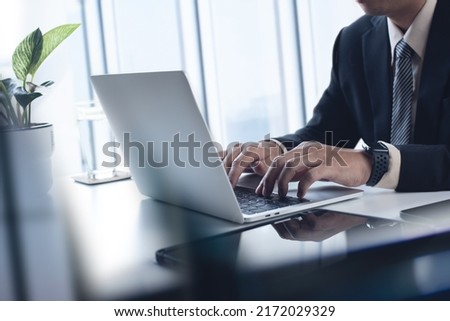 Asian business man working on laptop computer at modern office. Businessman in black suit working and typing on laptop keyboard, surfing the internet, digital tablet on office table, close up Royalty-Free Stock Photo #2172029329