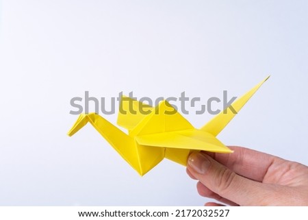 A hand holding a paper yellow bird on a light background. Paper crane as a symbol of peace. Paper origami. Paper crafts with children.